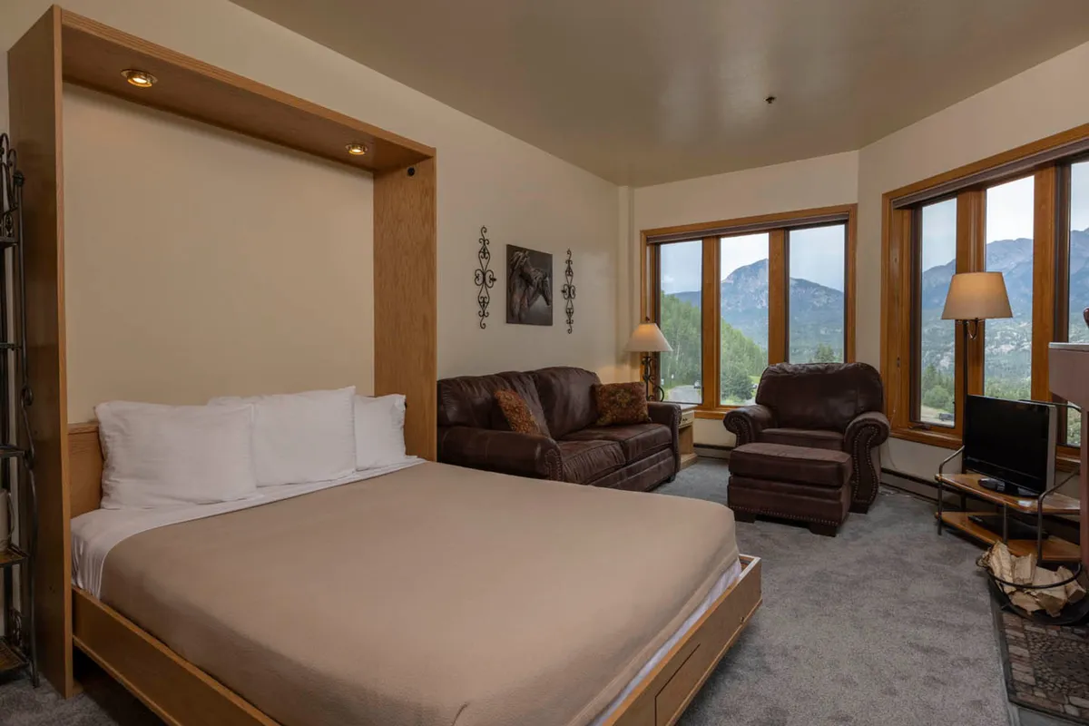 A serene bedroom featuring a king-size bed dressed in plush linens. Large windows let in natural light and offer scenic mountain views. The space includes a cozy seating area, perfect for relaxing with a book or enjoying the peaceful atmosphere.