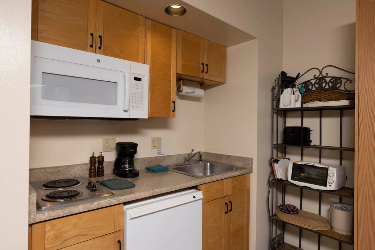This image provides a close-up of the kitchenette, featuring essential appliances such as a microwave, coffee maker, sink, stove, and open shelving. The setup invites guests to share a cup of coffee or cook a favorite meal, reinforcing the section’s focus on comfort and togetherness.