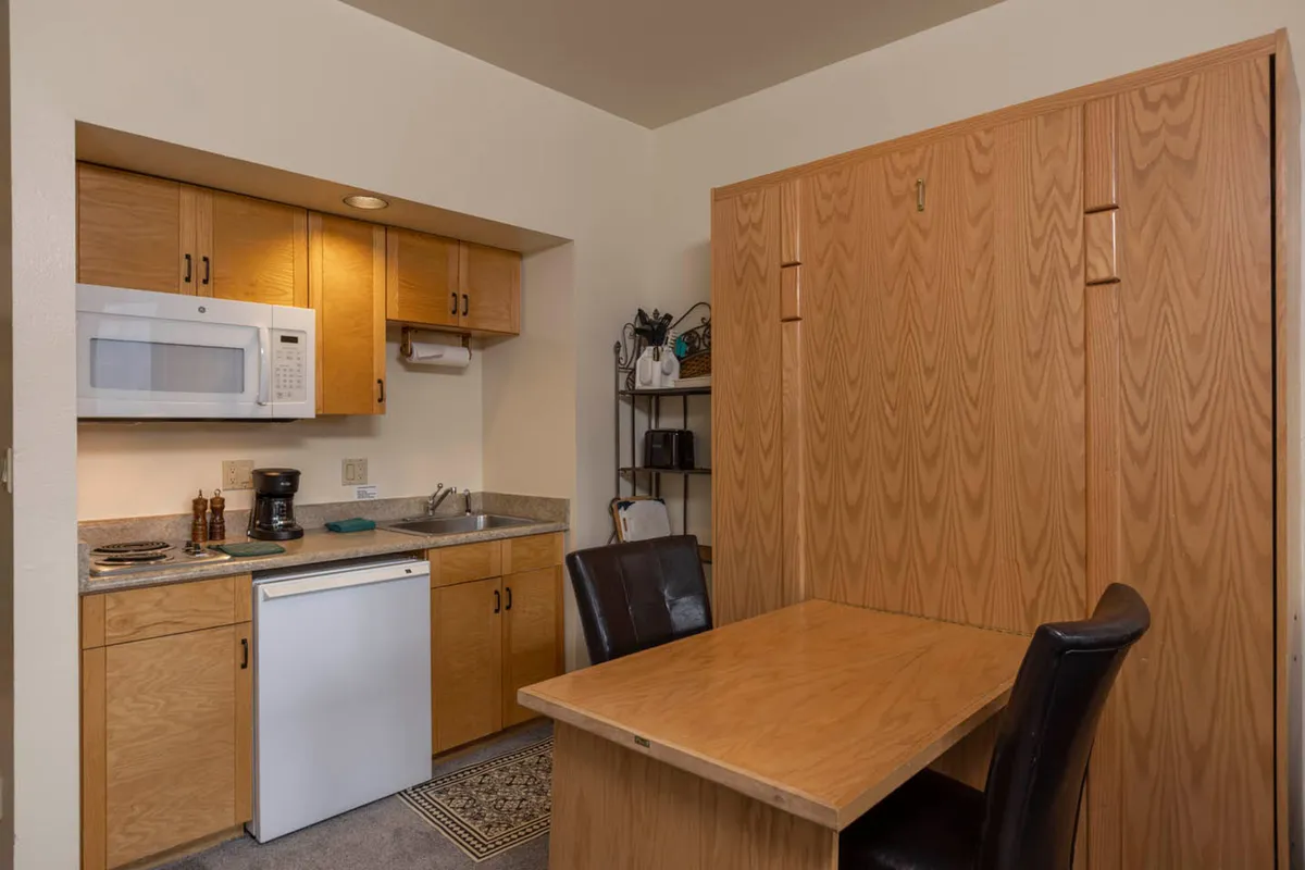 A practical kitchenette setup includes a fold-down table and black chairs, blending seamlessly into the open-plan living area. The space is both functional and charming, with subtle decor touches that enhance the sense of warmth and convenience.