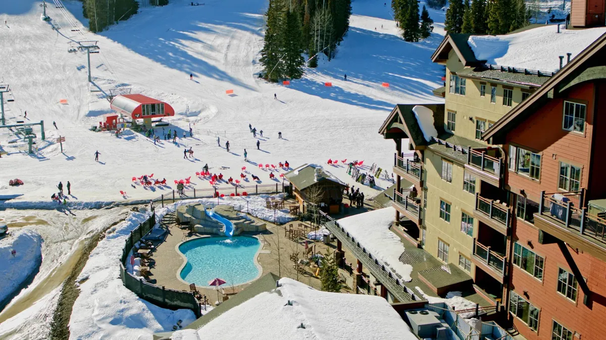 This outdoor scene features a swimming pool situated near snow-dusted ski slopes, with a ski lift and lodge visible in the background. Guests can be seen relaxing by the pool, with the ambiance blending recreation and relaxation against an adventurous mountain backdrop.